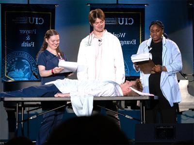 Stand-up comedian Jack Horchler is lying down for this skit written by Joel Baumgarten (center). His "assistants" are Marithe Imbolo-Yolinga (left) and Riley Jones. (Photo by Noah Allard))